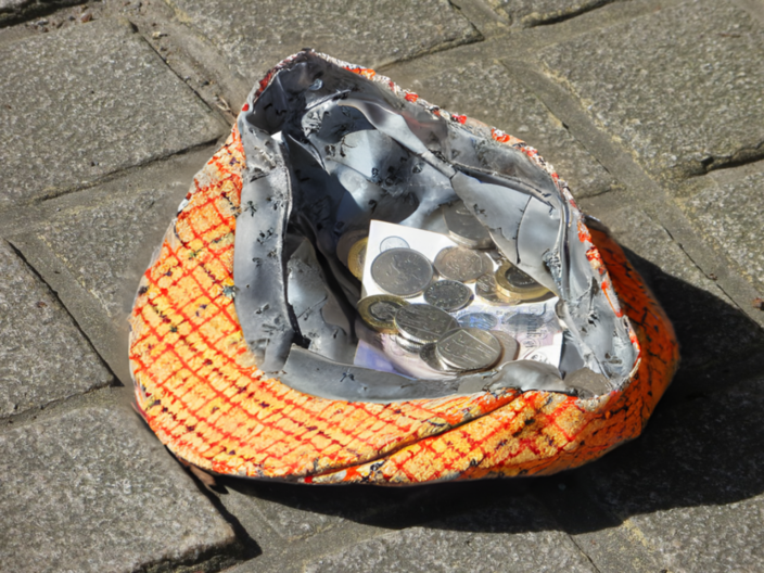 Man sieht eine Kappe oder Mütze auf dem Boden mit einigen Geldstücken darin