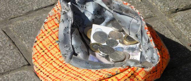 Man sieht eine Kappe oder Mütze auf dem Boden mit einigen Geldstücken darin