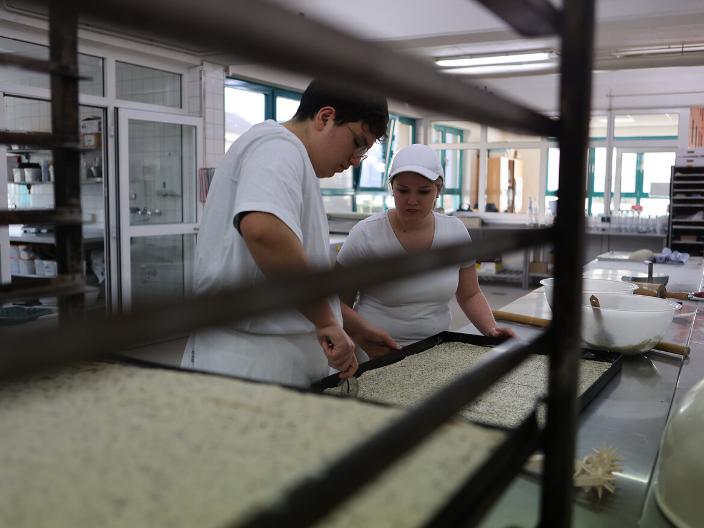 Ein Bäcker und eine Bäckerin bei der Arbeit in der Backstube