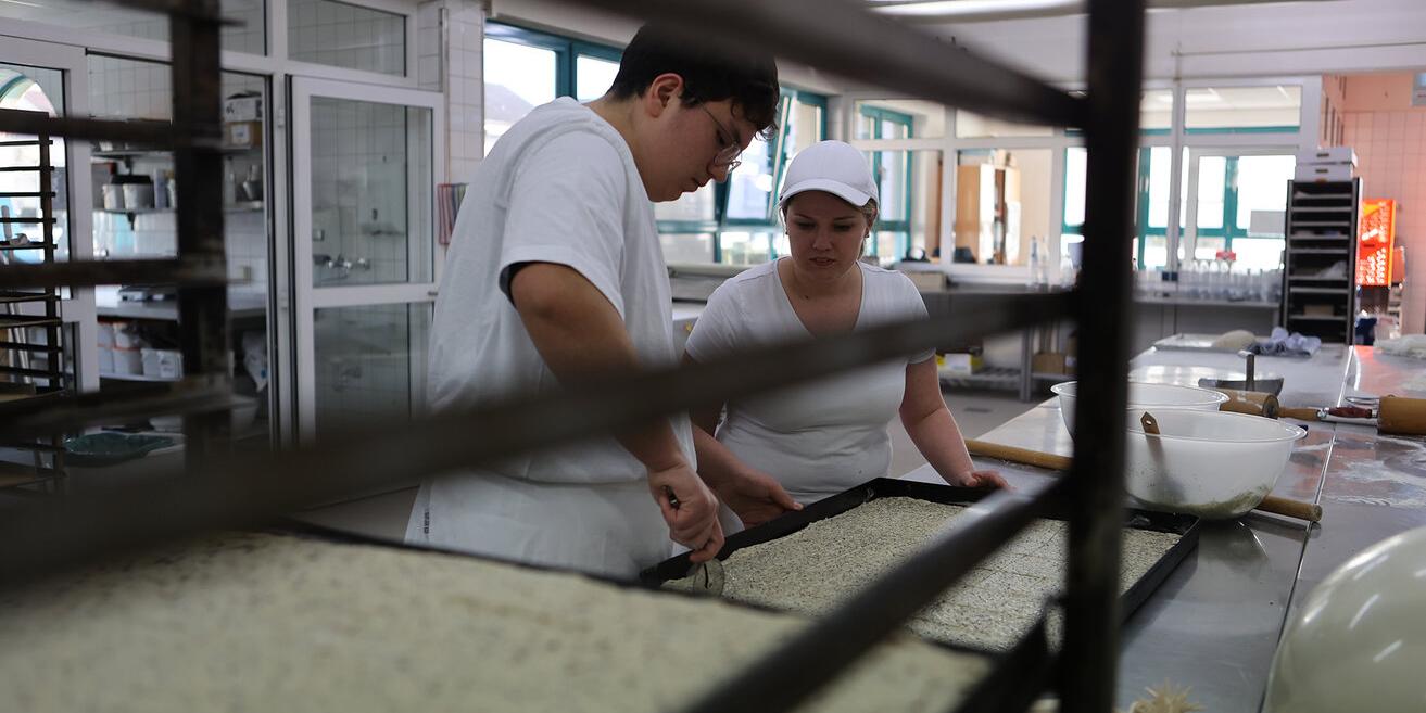 Ein Bäcker und eine Bäckerin bei der Arbeit in der Backstube