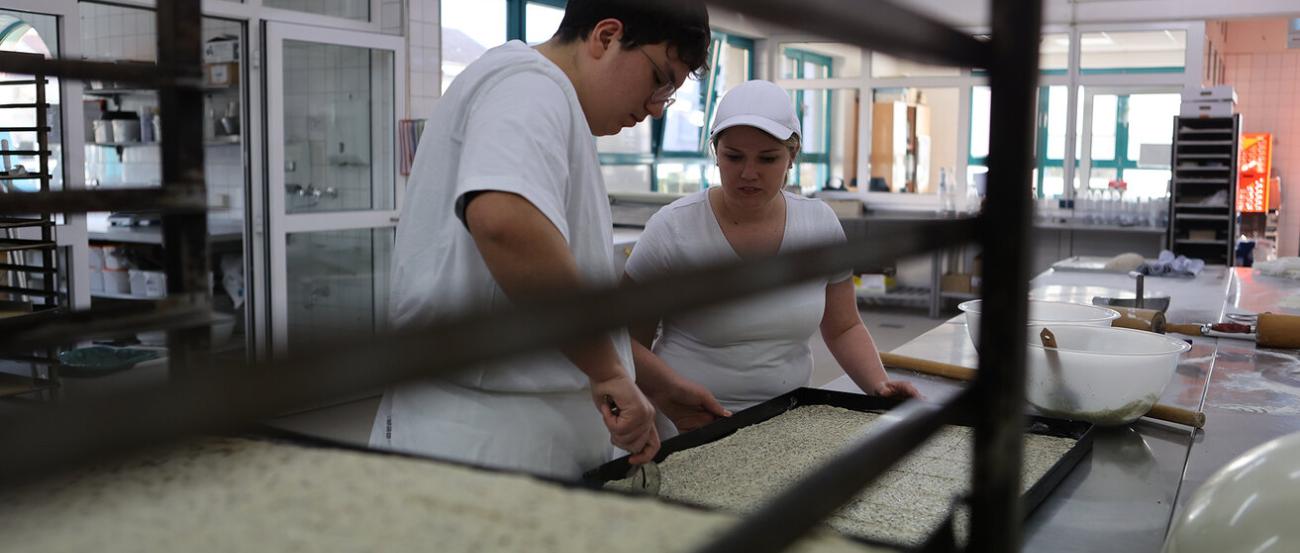 Ein Bäcker und eine Bäckerin bei der Arbeit in der Backstube