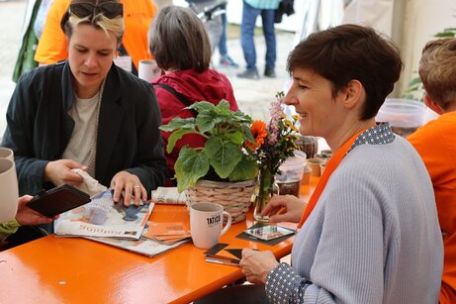 Menschen sitzen an einem orangenen Tisch und schauen Kolping-Infomaterial an