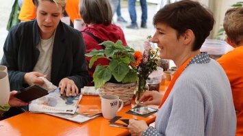 Menschen sitzen an einem orangenen Tisch und schauen Kolping-Infomaterial an