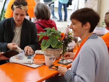 Menschen sitzen an einem orangenen Tisch und schauen Kolping-Infomaterial an