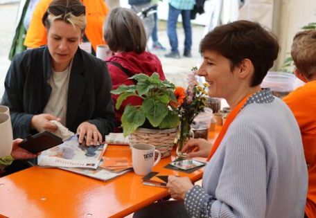 Menschen sitzen an einem orangenen Tisch und schauen Kolping-Infomaterial an
