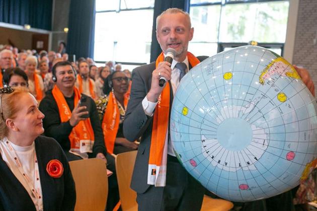 Mann mit einer großen Weltkugel unter dem Arm spricht vor einer Versammlung