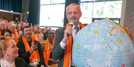 Mann mit einer großen Weltkugel unter dem Arm spricht vor einer Versammlung