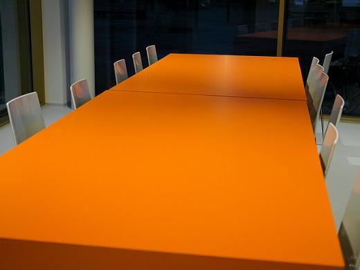 Man sieht einen orangenen Besprechungstisch mit Stühlen