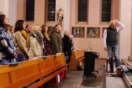 Ein gemischter Chor probt in einer Kirche, der Chorleiter gibt Anweisung zu einer Einsingübung.