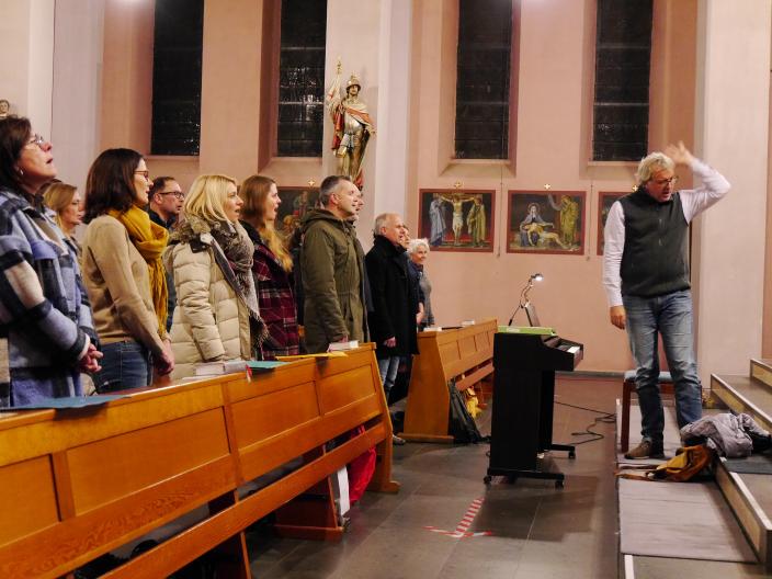 Ein gemischter Chor probt in einer Kirche, der Chorleiter gibt Anweisung zu einer Einsingübung.