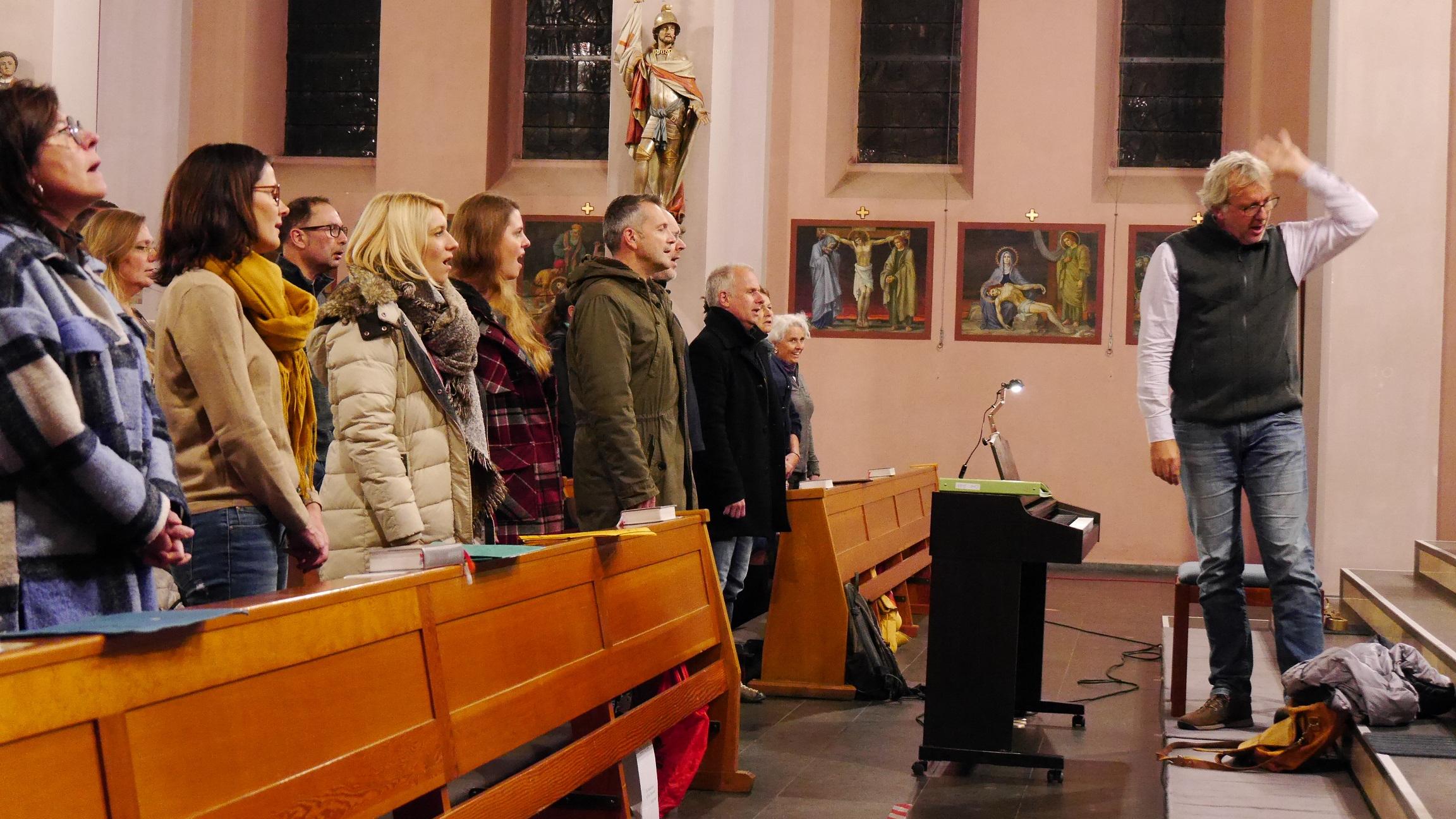Ein gemischter Chor probt in einer Kirche, der Chorleiter gibt Anweisung zu einer Einsingübung.